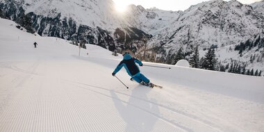 Skifahrer carvt über die frisch präparierte Piste. Im Hintergrund das Bergpanorama. | © Bergbahnen Brandnertal, Timo Hummel